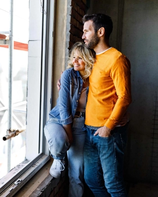 Glueckliches Paar schaut aus dem Fenster ihres Wohneigentums, welches sich noch im Bau befindet.